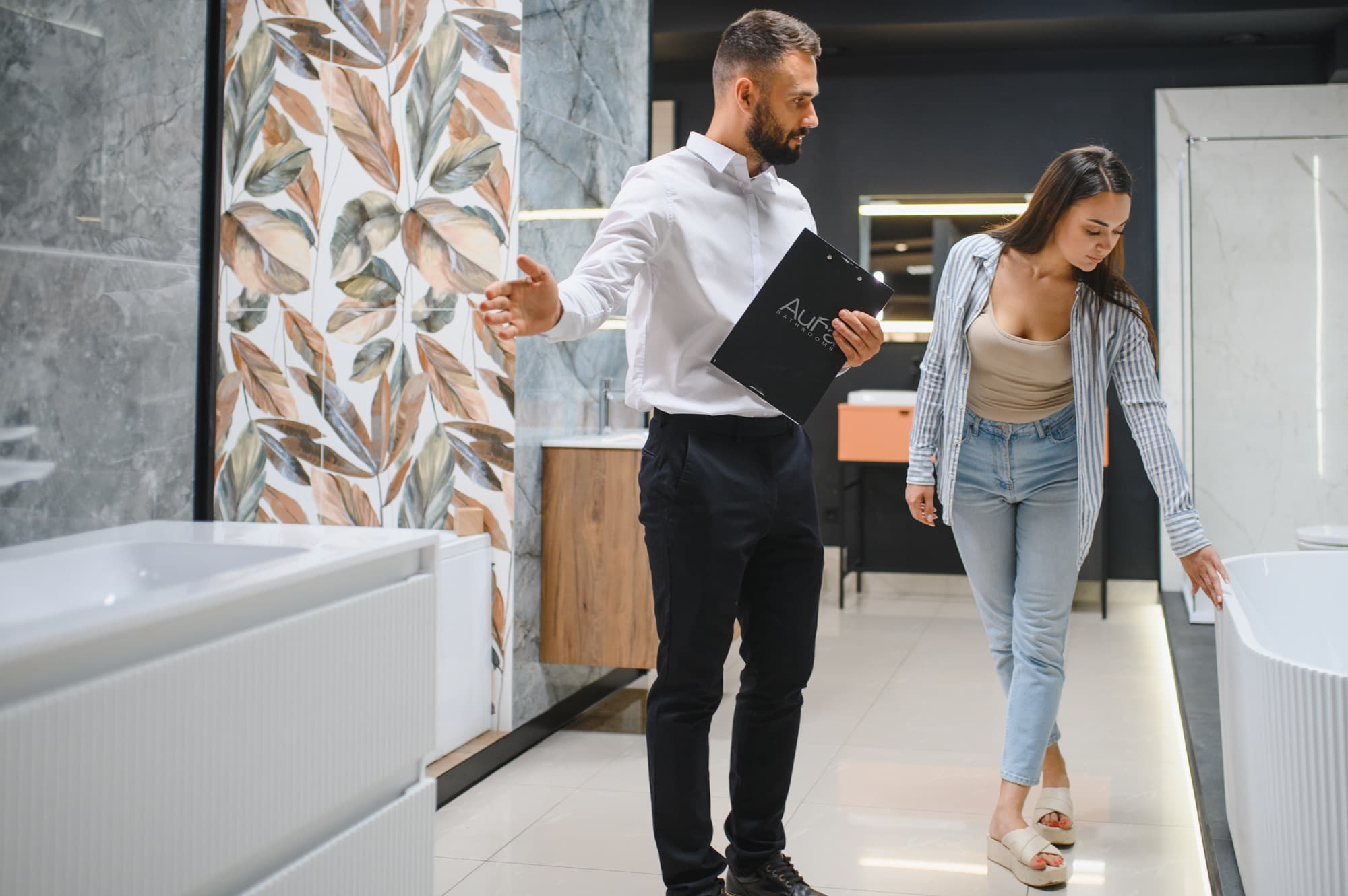 A designer with a clipboard showing a customer around a bathroom showroom