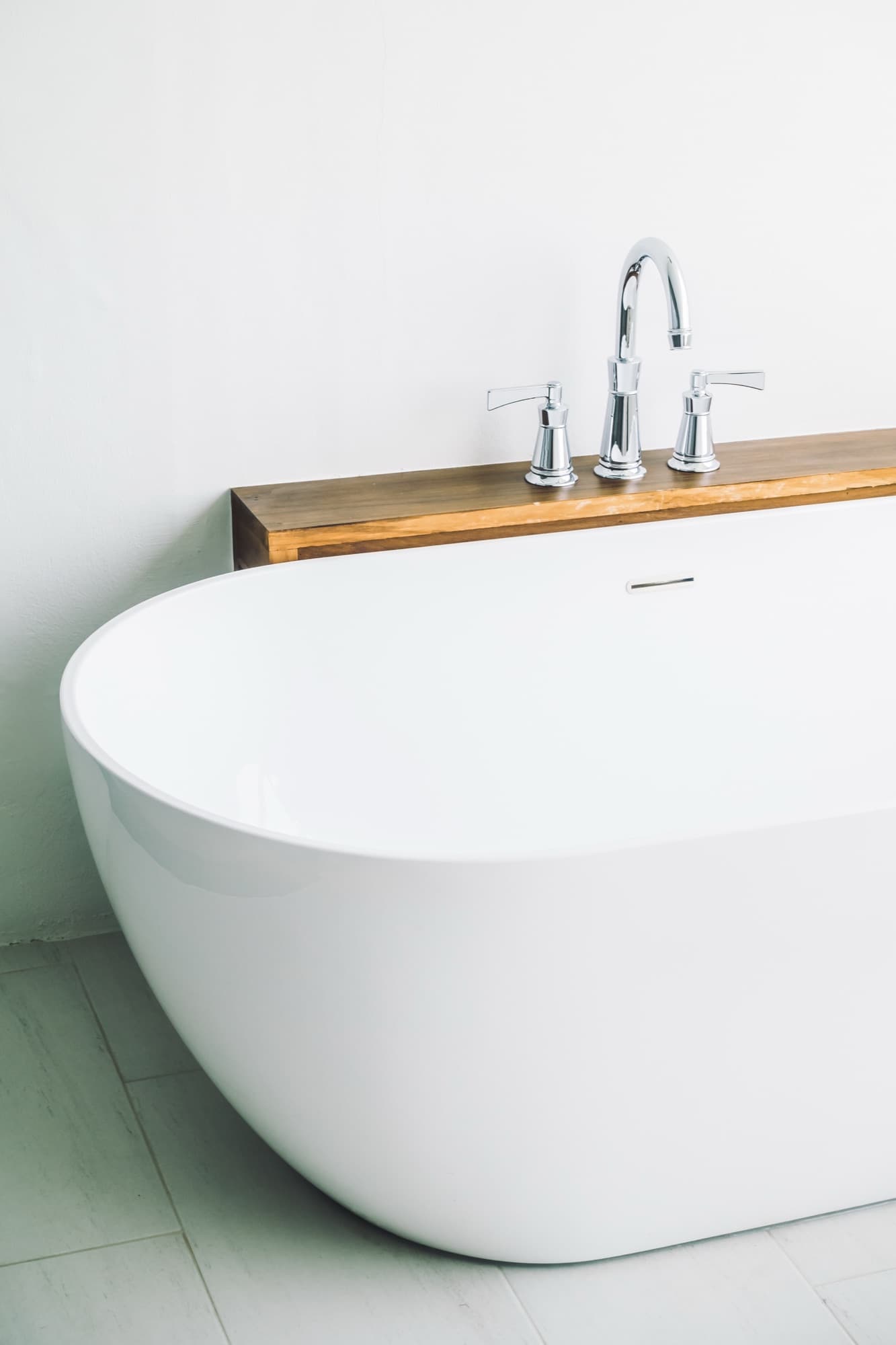 A freestanding bath with chrome pillar taps set on a timber shelf