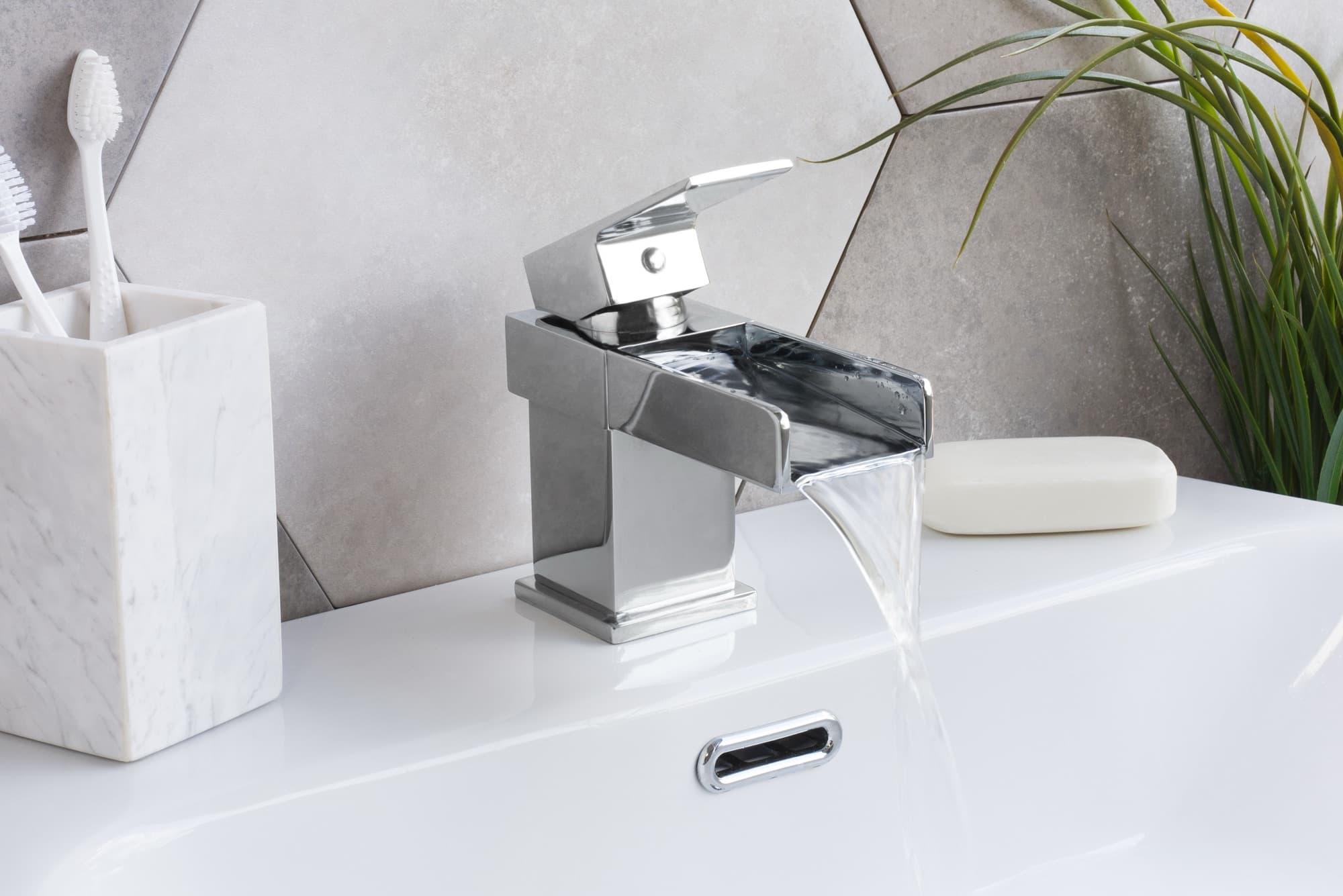 A chrome waterfall basin mixer running over a white basin